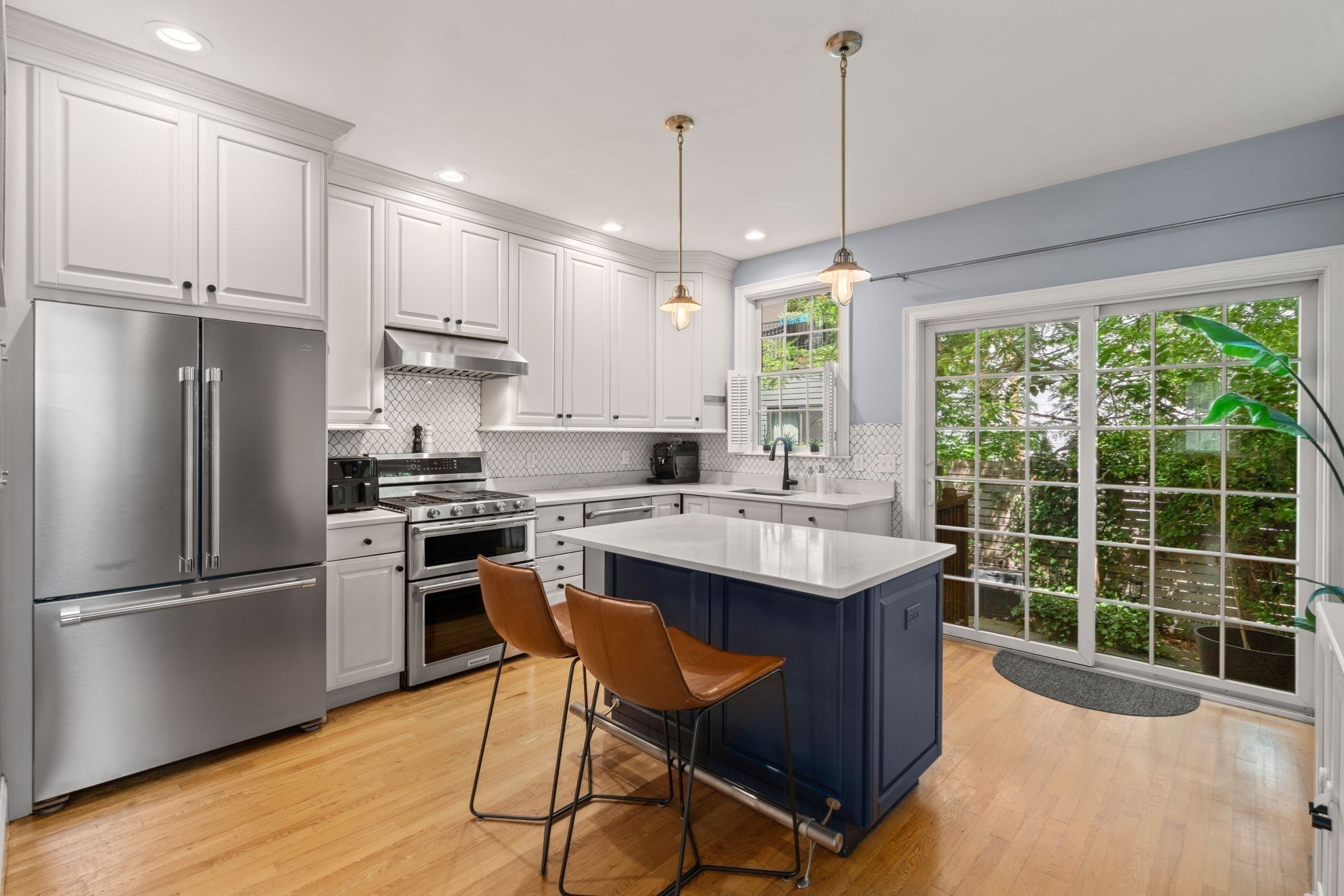 Kitchen with a navy island, white cabinetry, stainless steel appliances, and glass doors overlooking greenery.