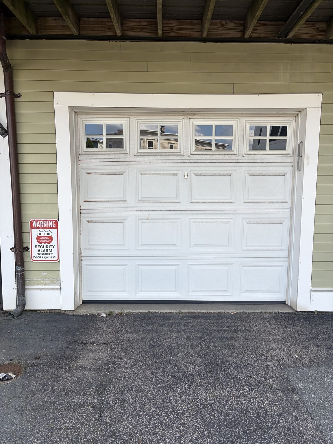 White paneled garage door with upper windows in pale green siding, beside a security alarm sign.