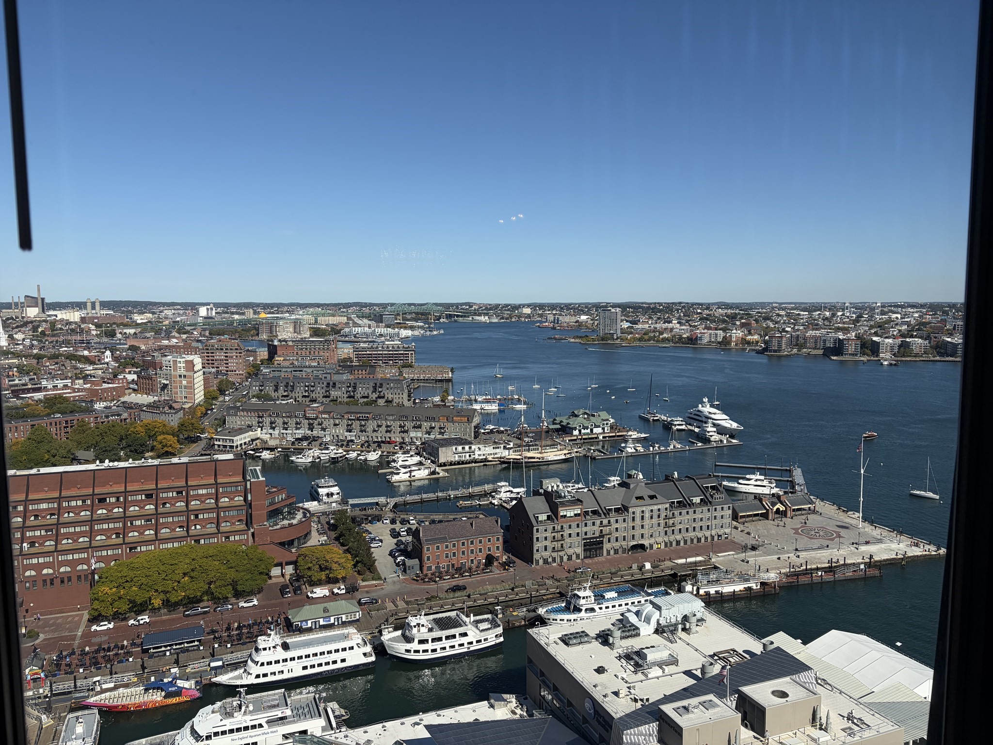 Urban harbor view with ferries, sailboats, waterfront buildings, and a distant skyline.