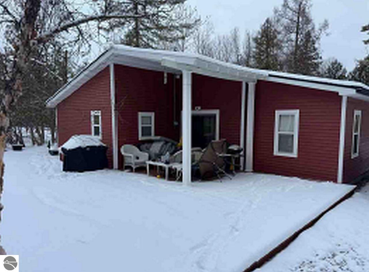 Red-sided house with a covered patio and outdoor furniture surrounded by deep snow.
