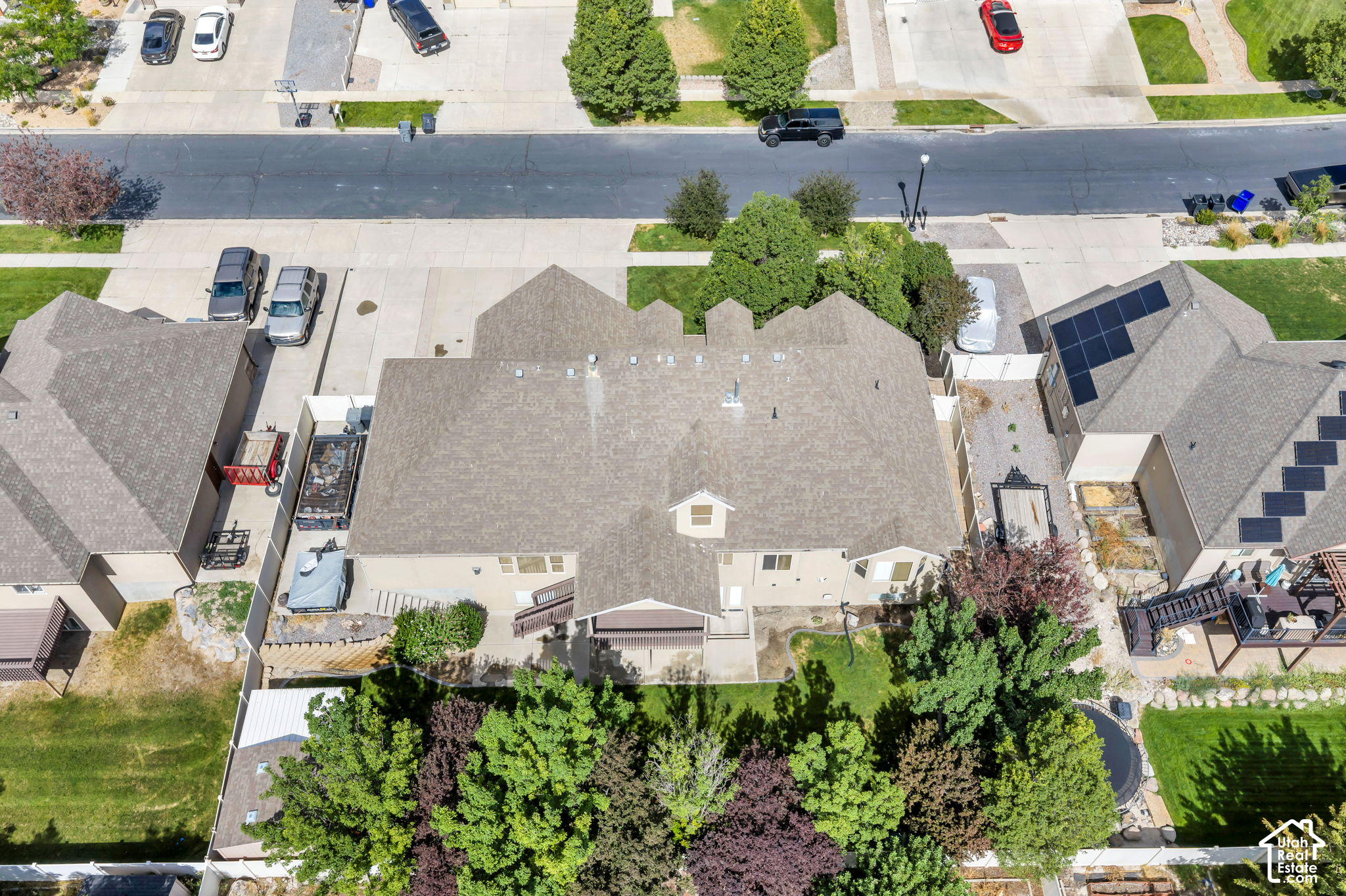 Aerial view of a beige home with a tree-filled backyard and neighboring homes along the street.