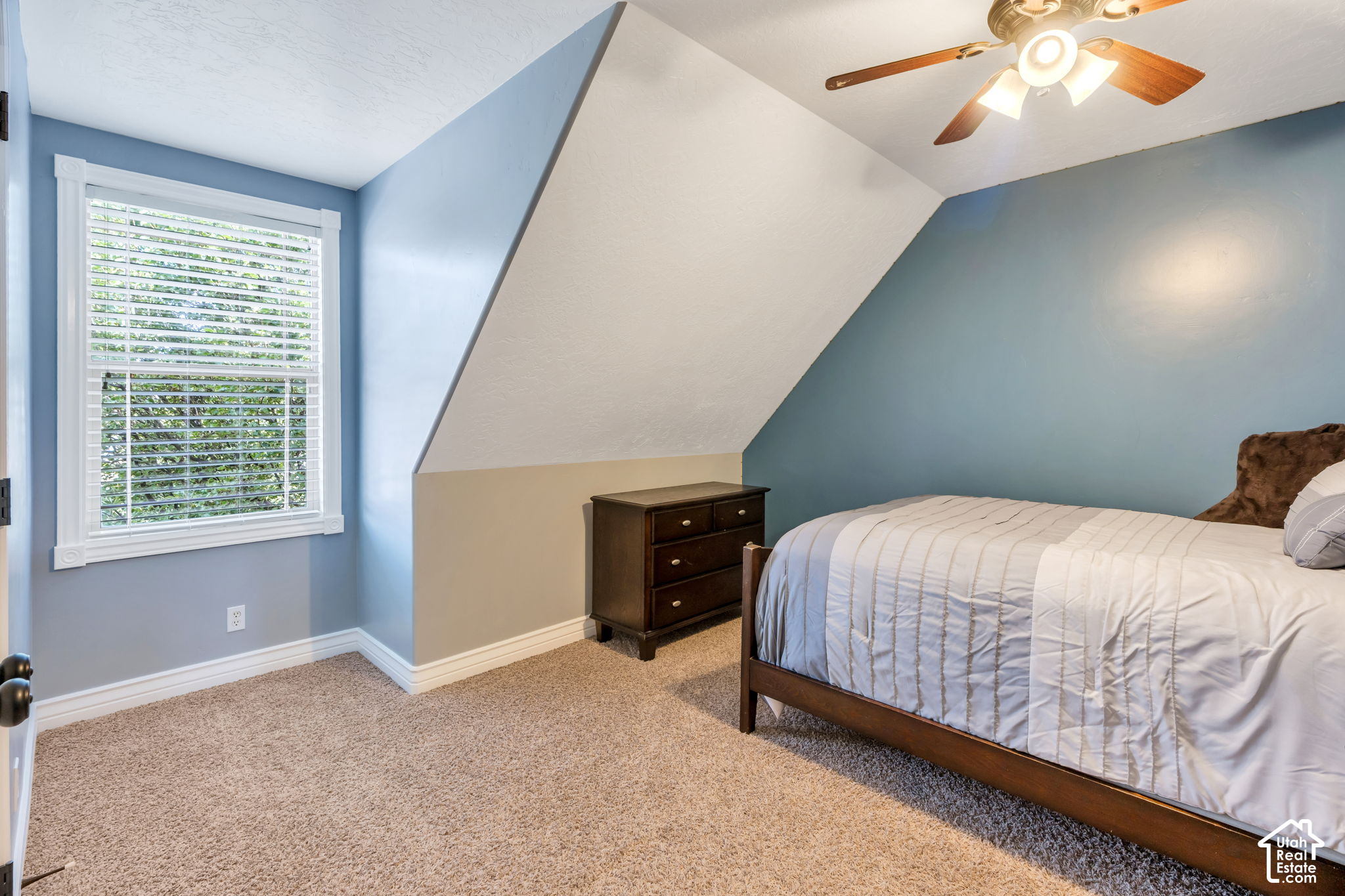 Bedroom with a sloped ceiling, blue walls, and a window with white blinds.