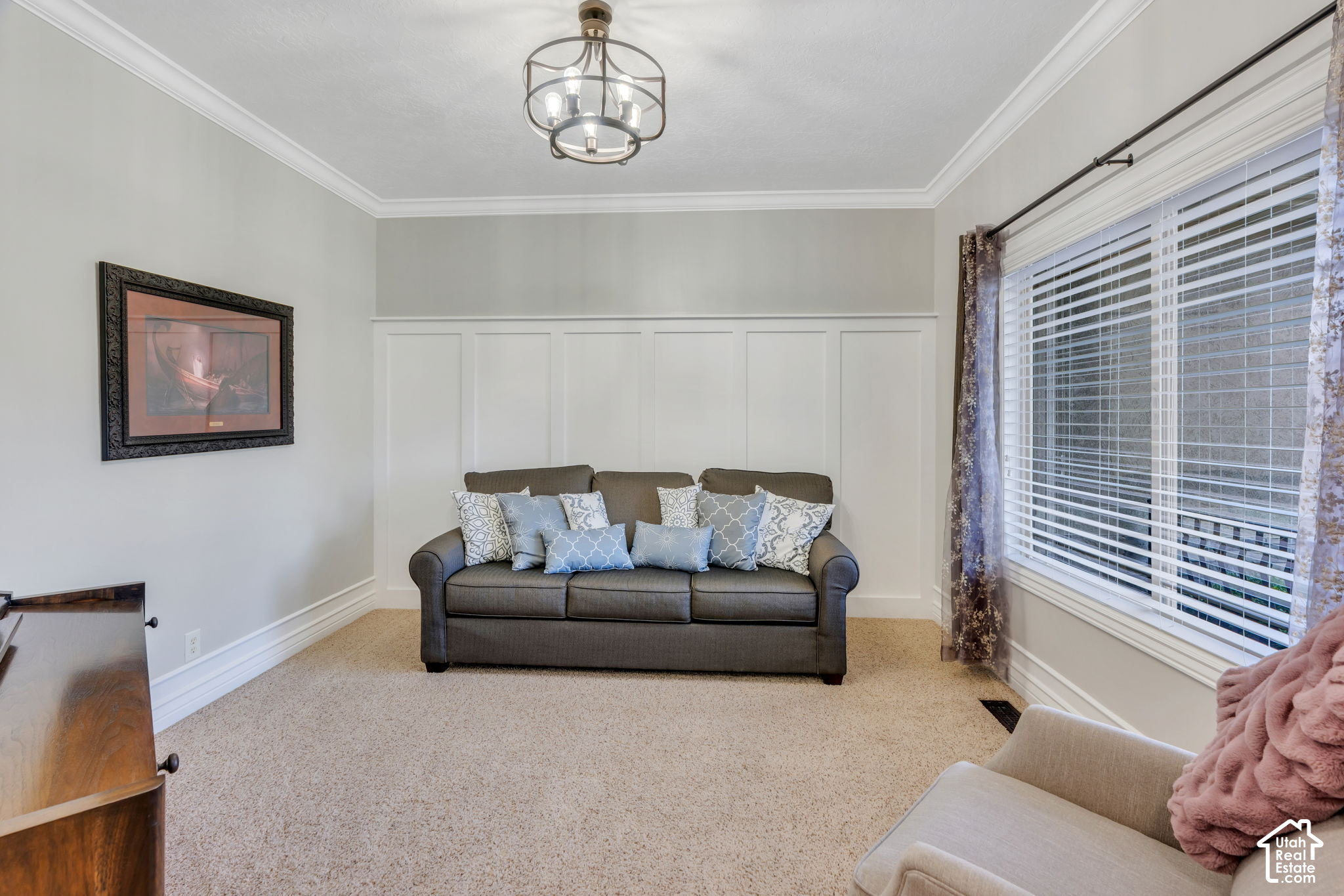 Furnished sitting room with a gray sofa, patterned pillows, paneled wall, and large window.