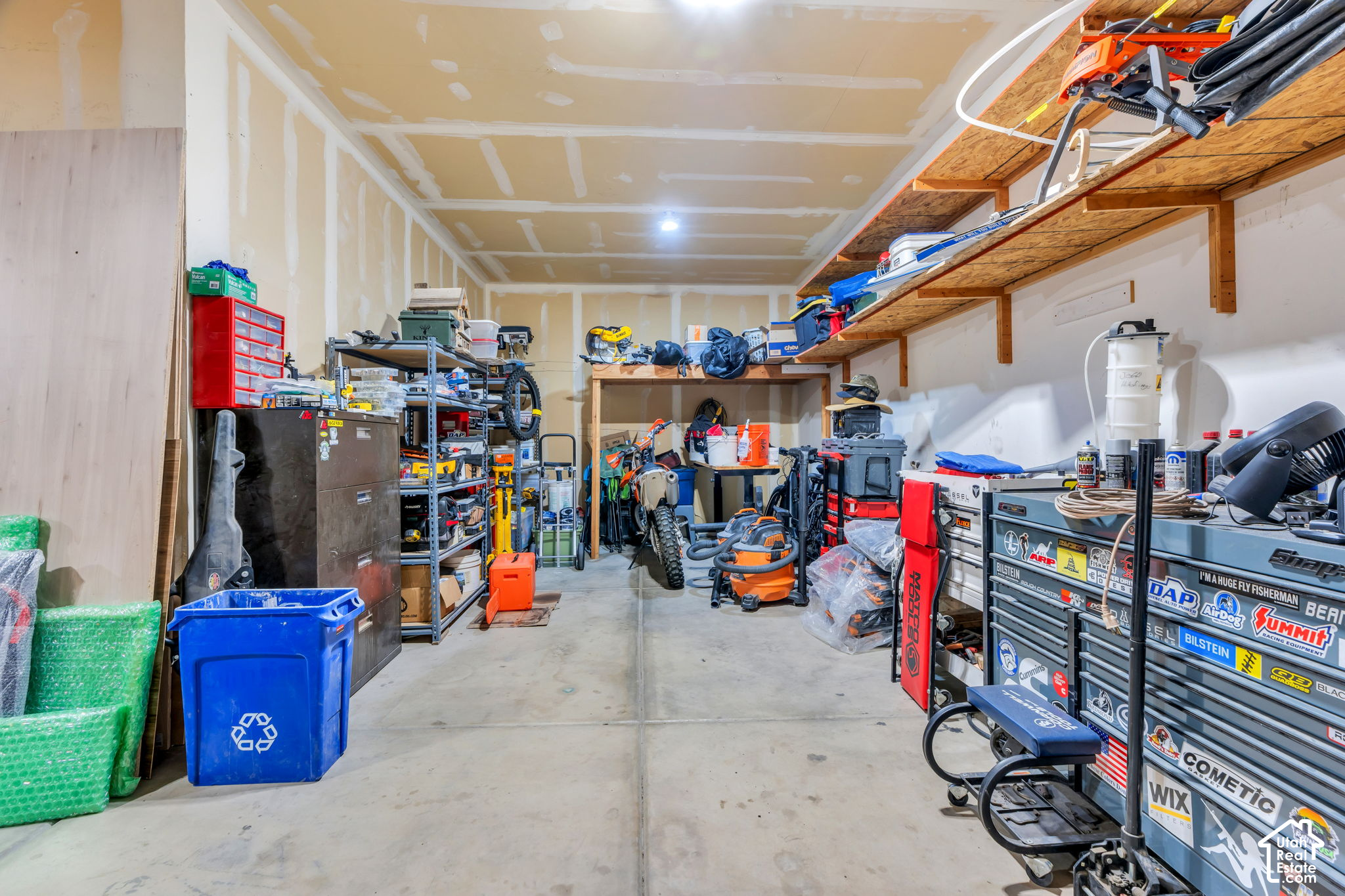 Garage workshop with tool chests, equipment, and unfinished drywall.