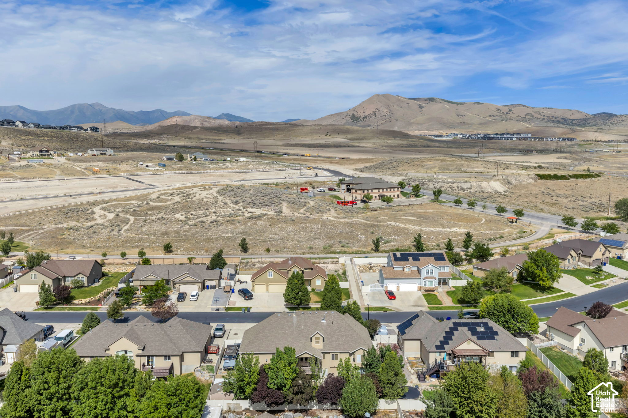 Aerial view of homes beside open land, with dry mountain ridges in the distance.