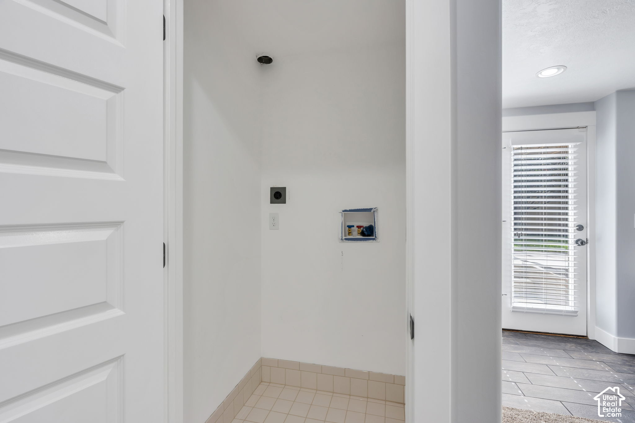 Empty laundry area with washer and dryer hookups beside a blind-covered exterior door.