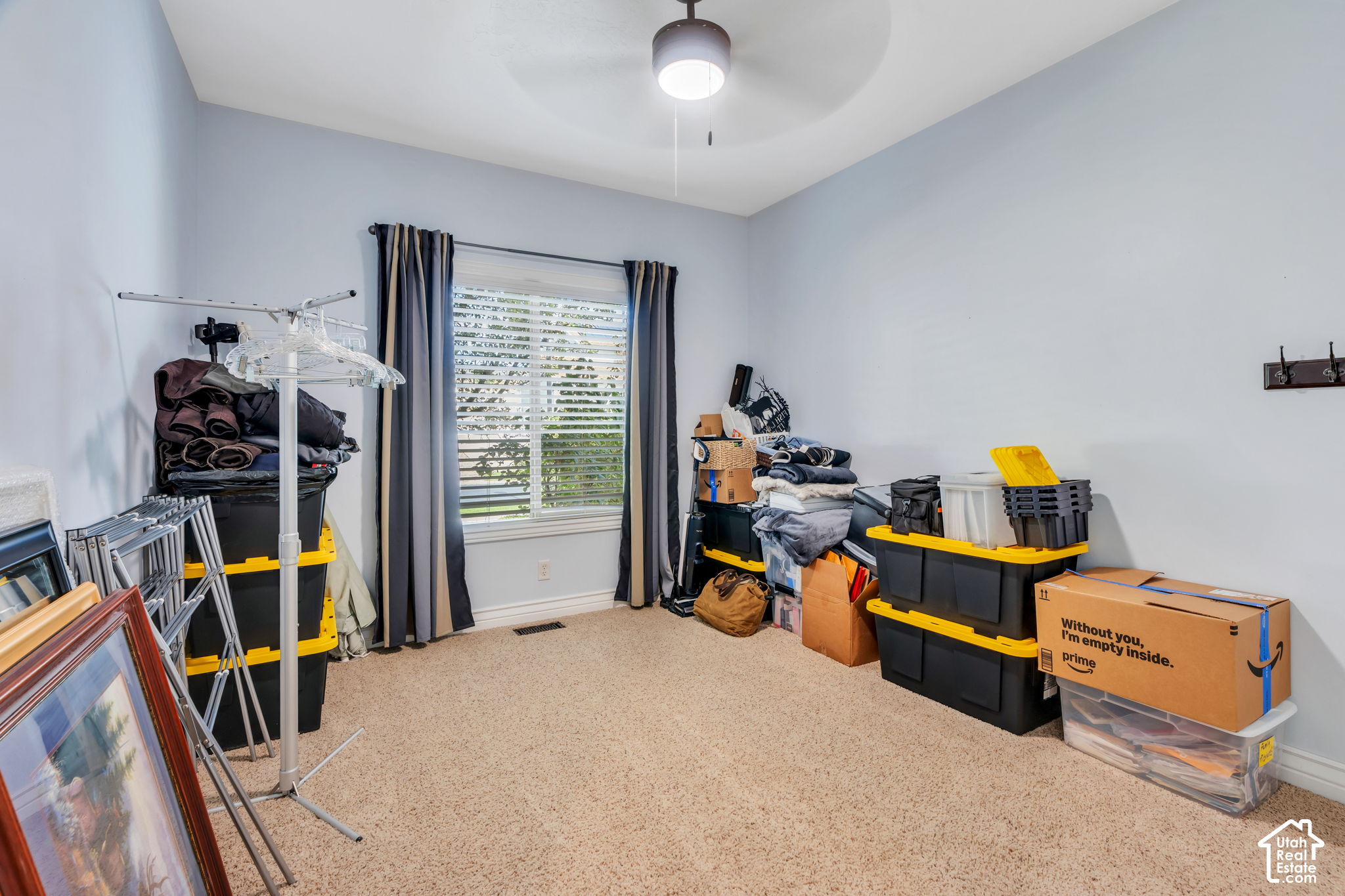 Carpeted storage room with stacked bins, boxes, framed pictures, and a window with blinds.
