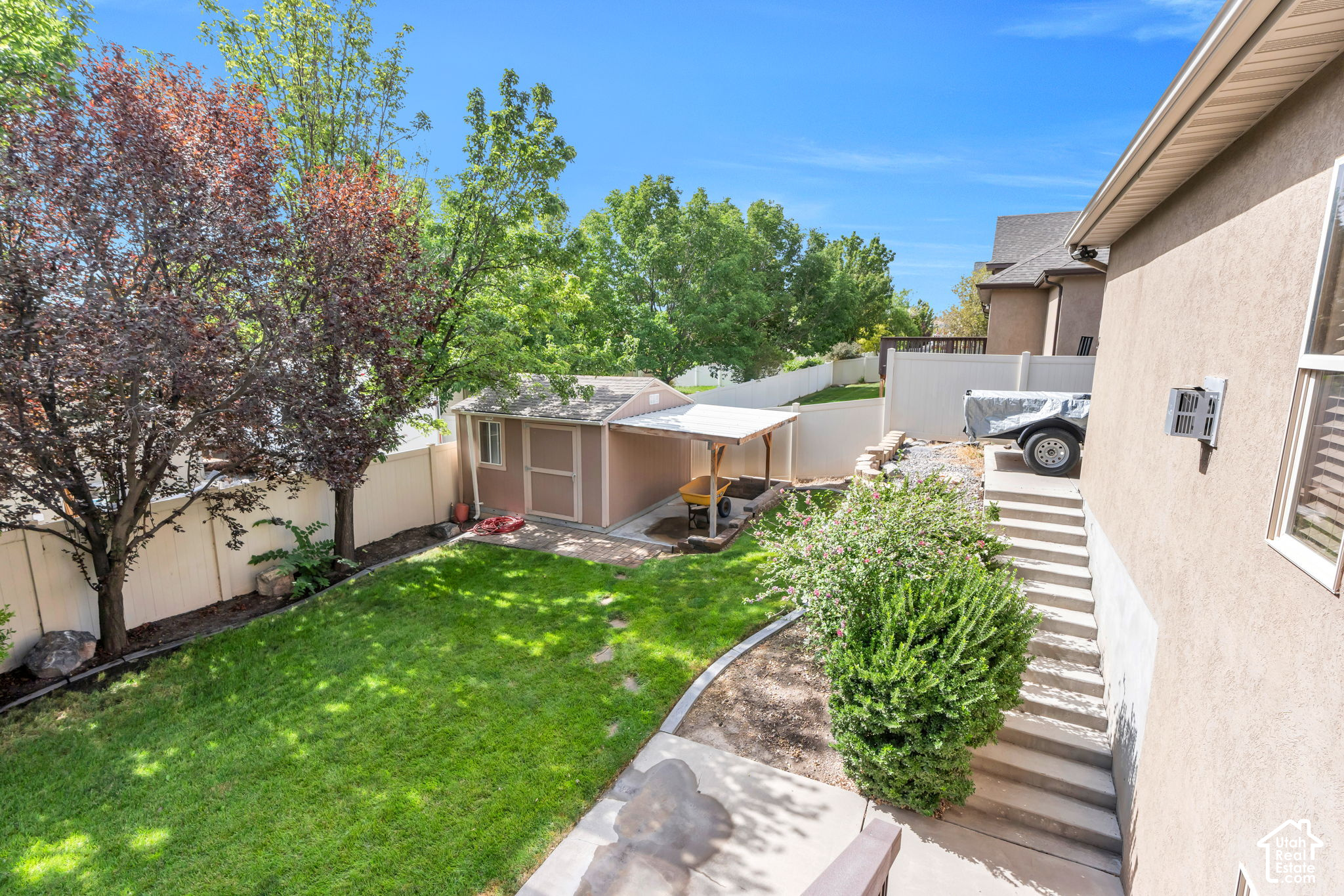Fenced backyard with a lawn, mature trees, and a small shed with a covered work area.