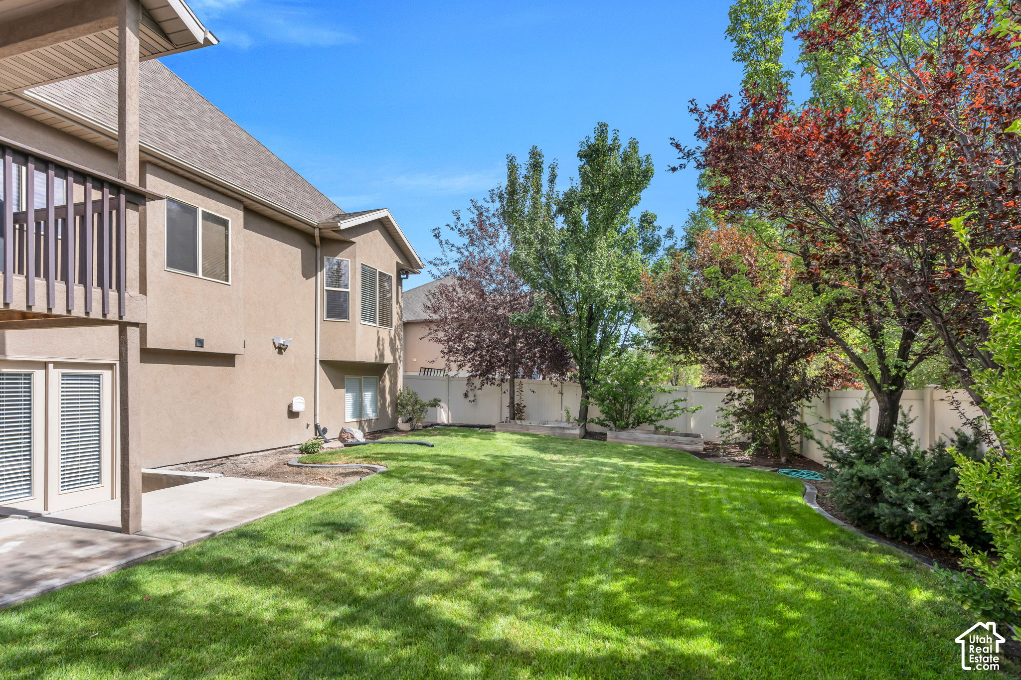 Fenced backyard with a broad lawn, mature trees, and a patio beside the home's rear exterior.