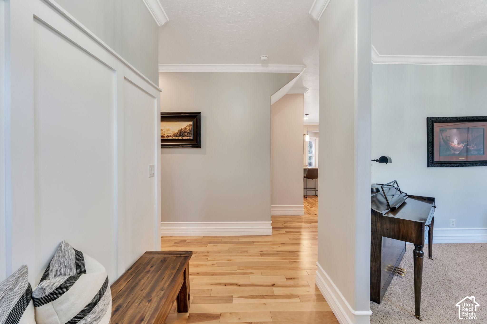 Furnished hallway with light wood floors, a wooden bench, and a glimpse of a carpeted sitting area.