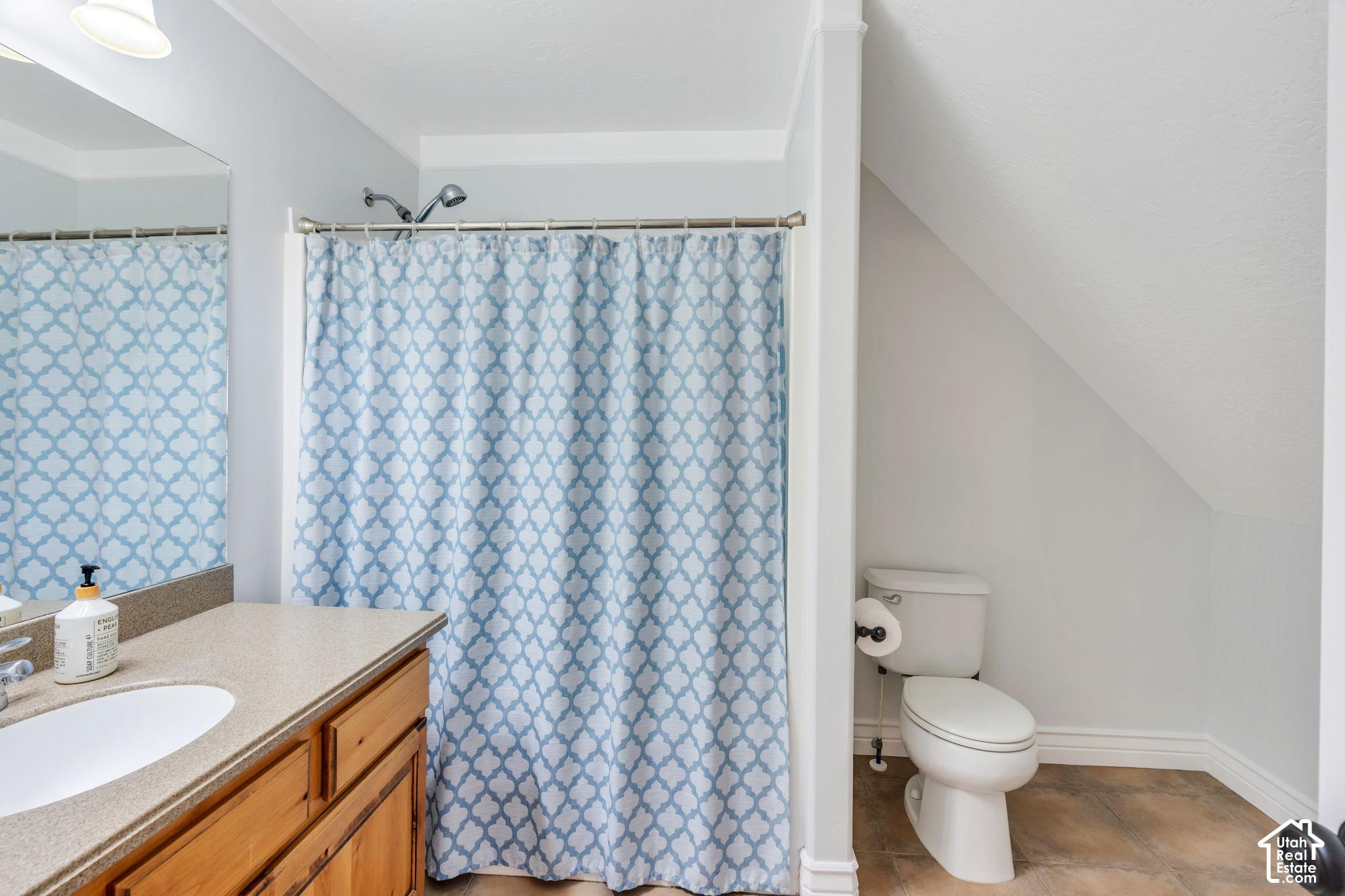 Bathroom with a wood vanity and blue-and-white patterned shower curtain beside a toilet.