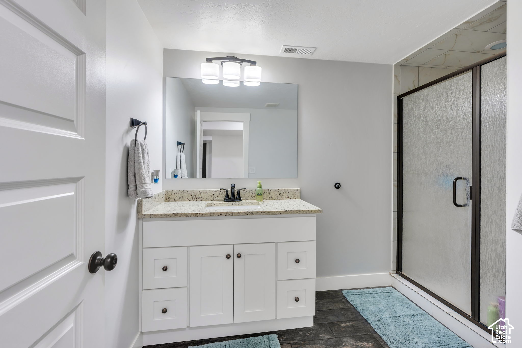 Bathroom with white vanity, speckled countertop, large mirror, and black-framed glass shower.