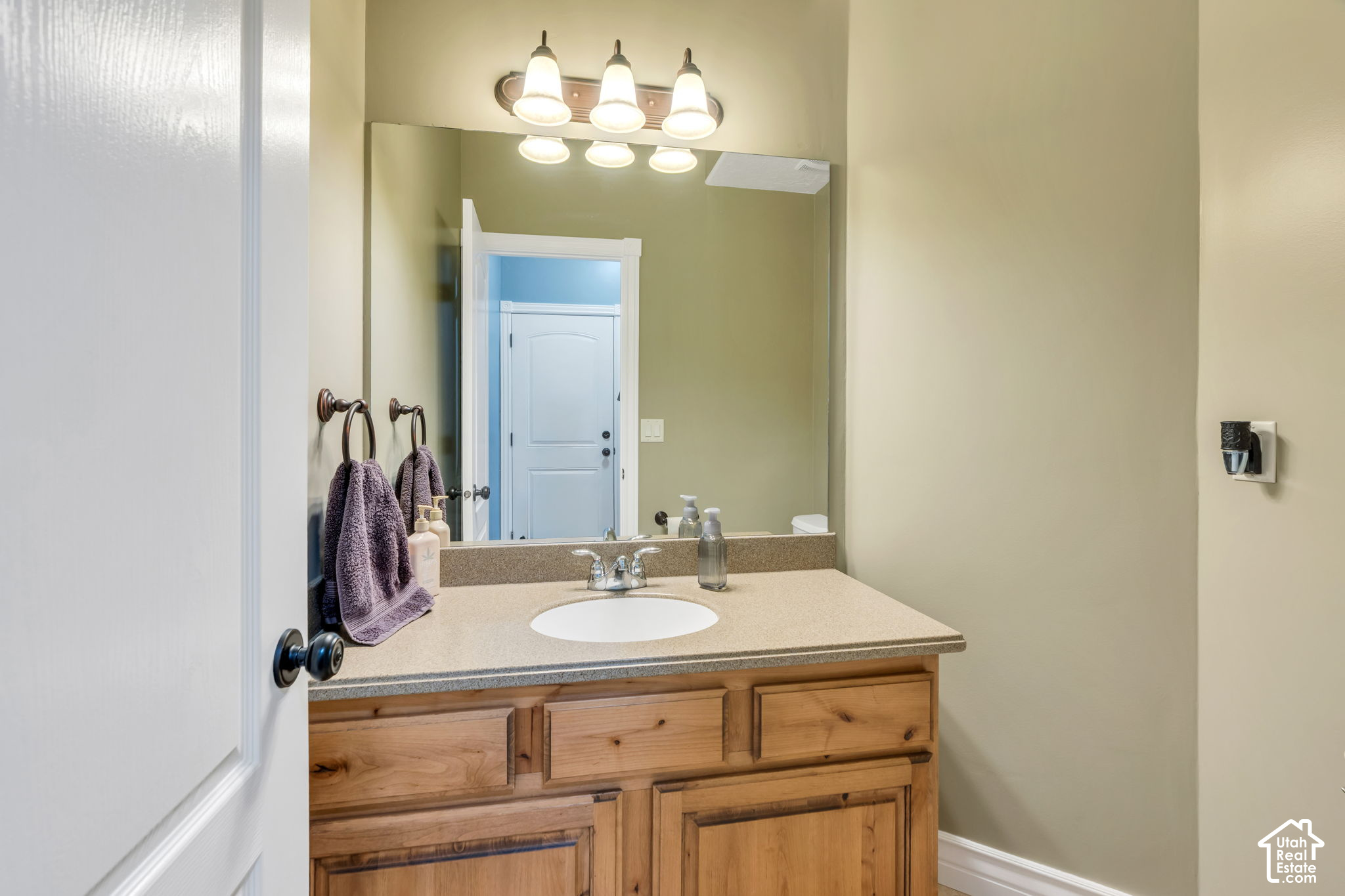 Bathroom vanity with a white sink, natural wood cabinets, and a large mirror.