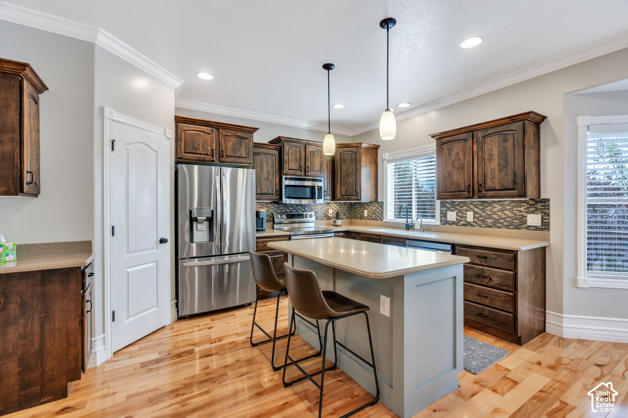 Kitchen with dark wood cabinets, stainless steel appliances, and a large island with two chairs.