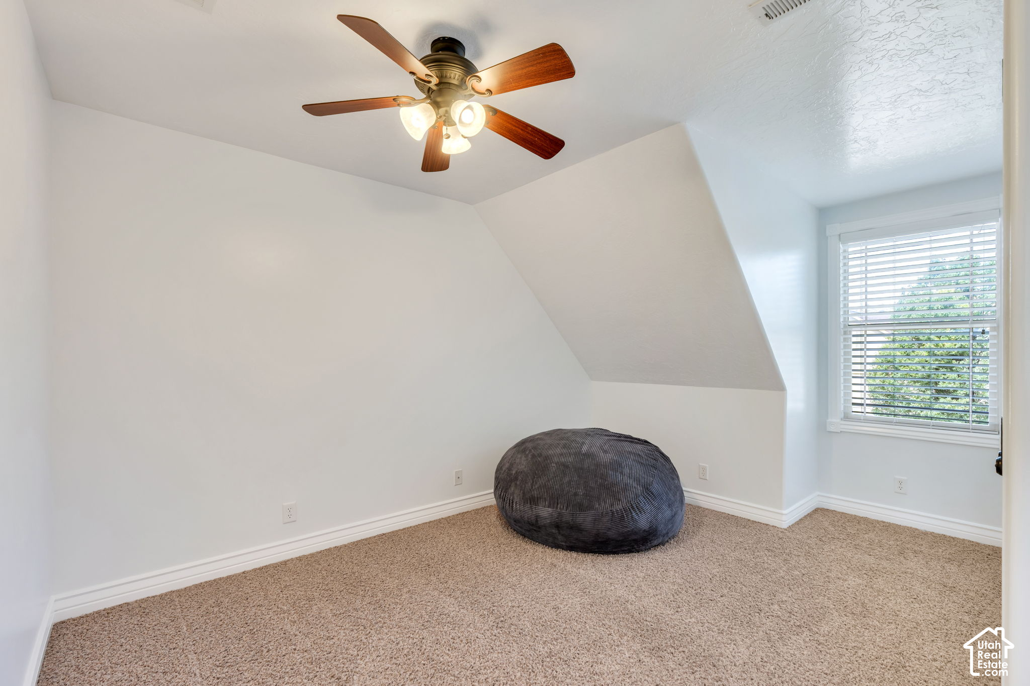 Upstairs room with a sloped ceiling, dark beanbag chair, carpet, and window with blinds.
