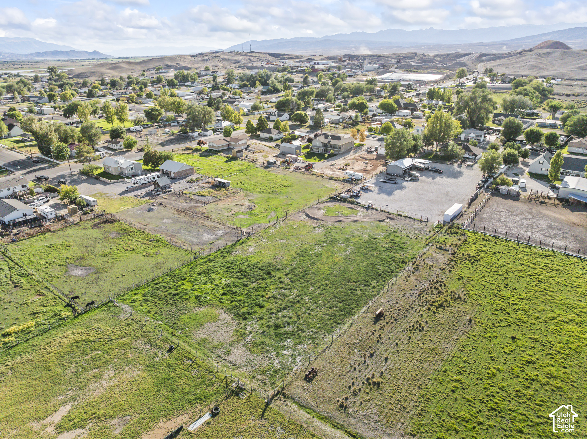 Fenced acreage with pasture, neighboring homes, a gravel lot, and distant mountains.