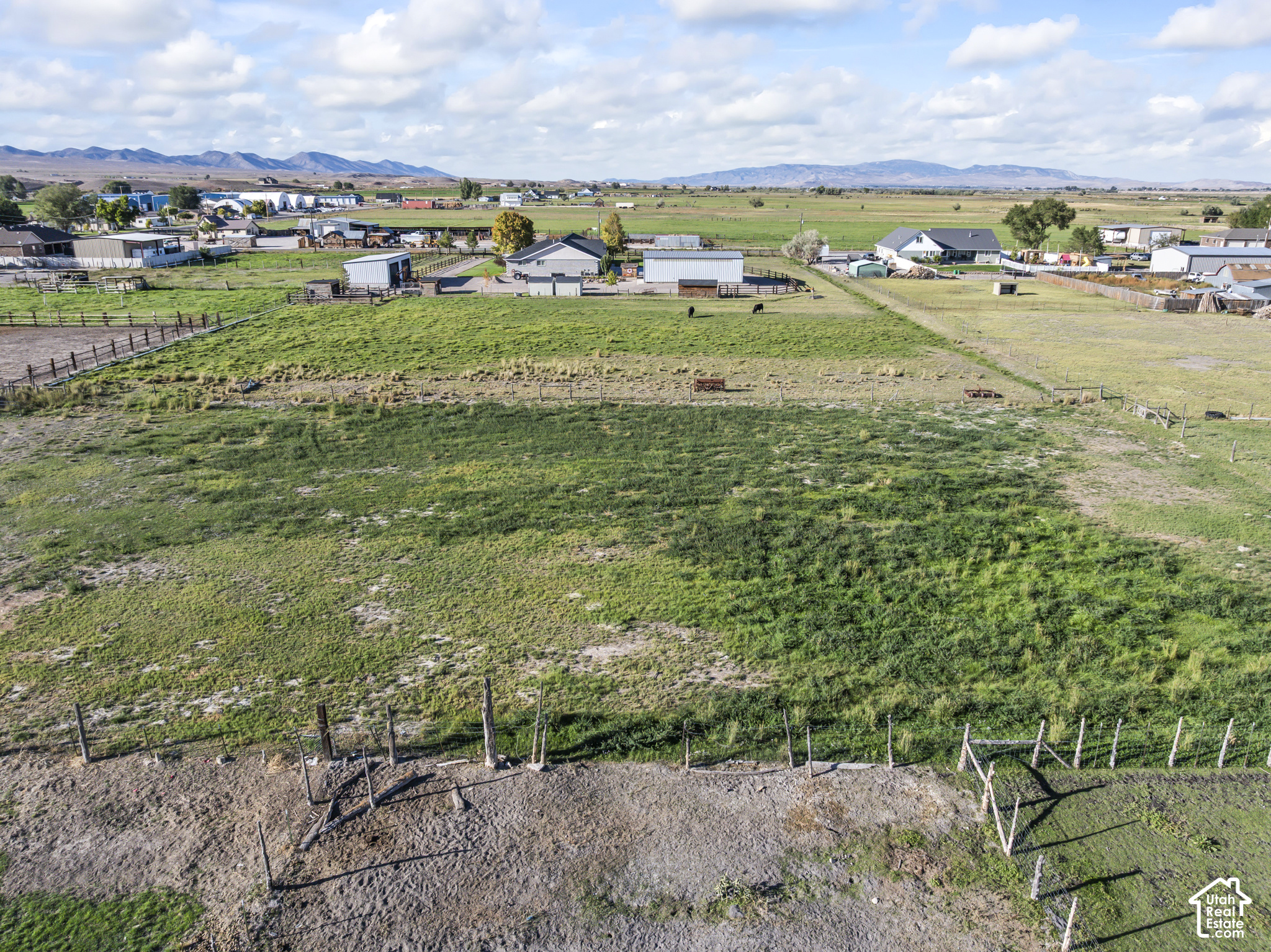 Aerial view of fenced green pastureland with farm buildings and distant mountains.