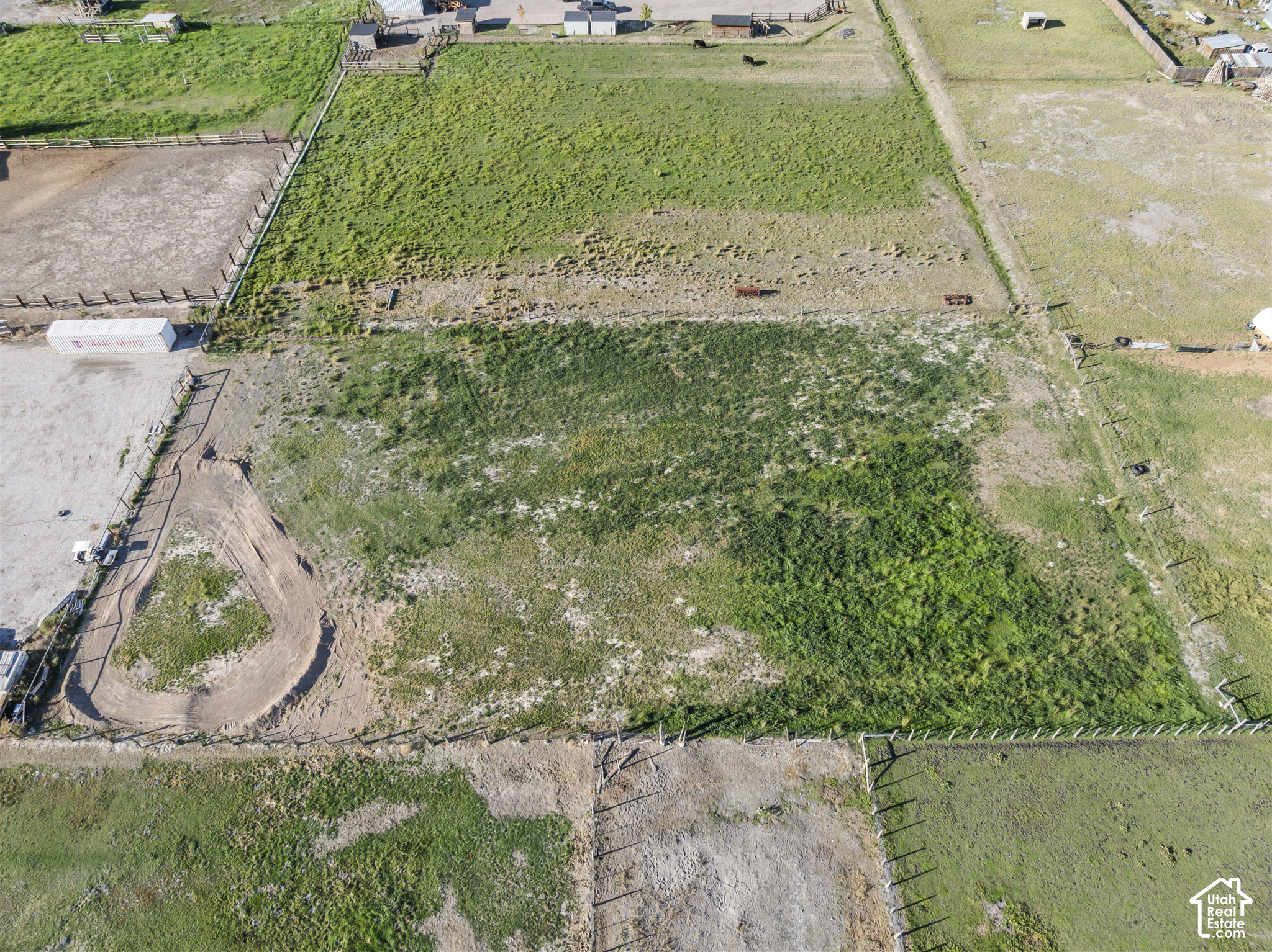 Aerial view of fenced pasture with paddocks, patchy grass, and a curved dirt track.