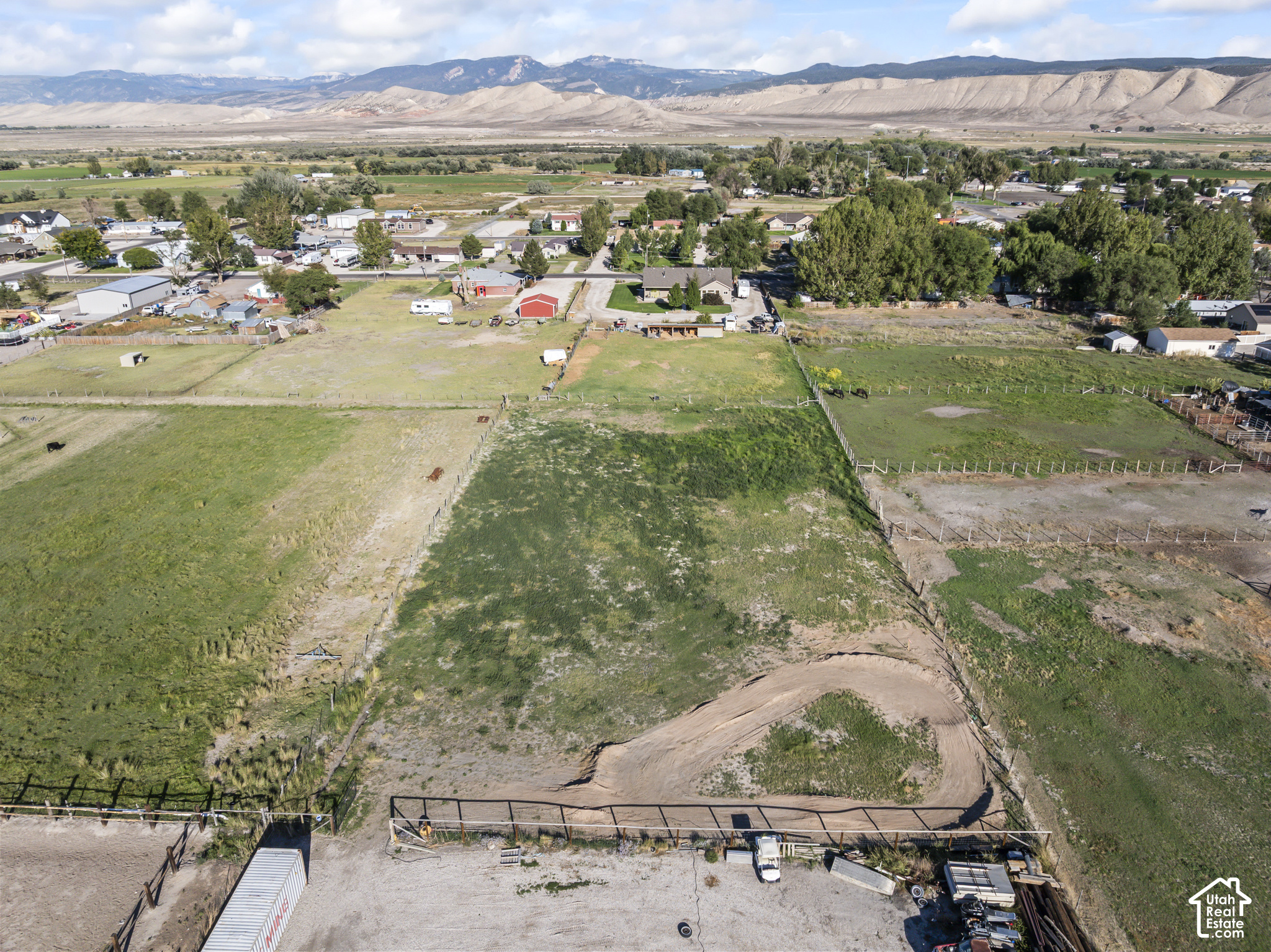 Fenced pastureland with a curving dirt track and mountain ranges in the distance.