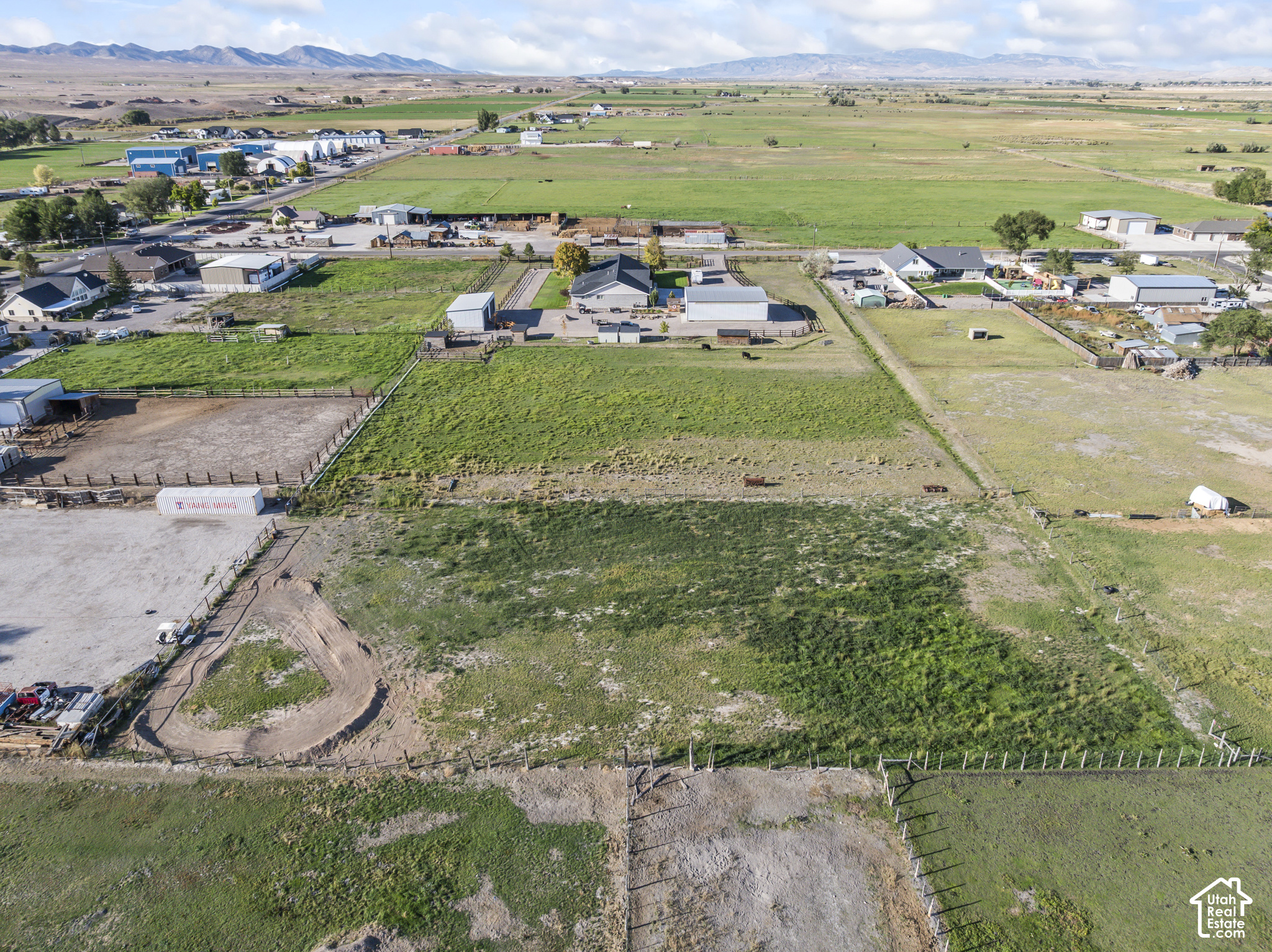 Aerial view of fenced rural pastureland and scattered buildings, with mountains in the distance.