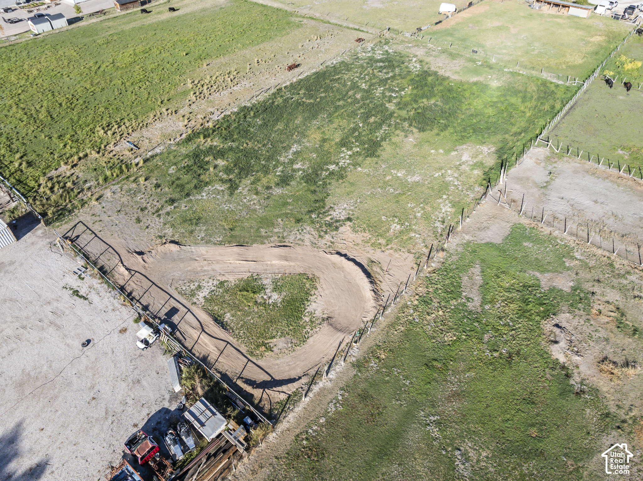 Aerial view of fenced pasture with a curved dirt track and livestock.