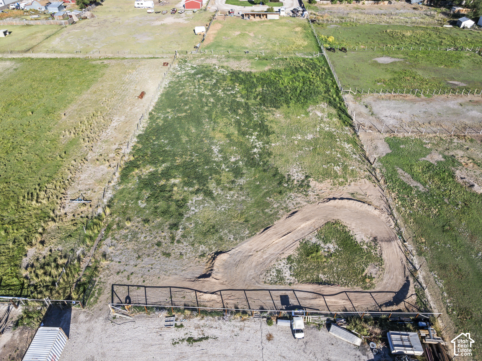 Fenced rural property with patchy grass and a curved dirt track, viewed from above.
