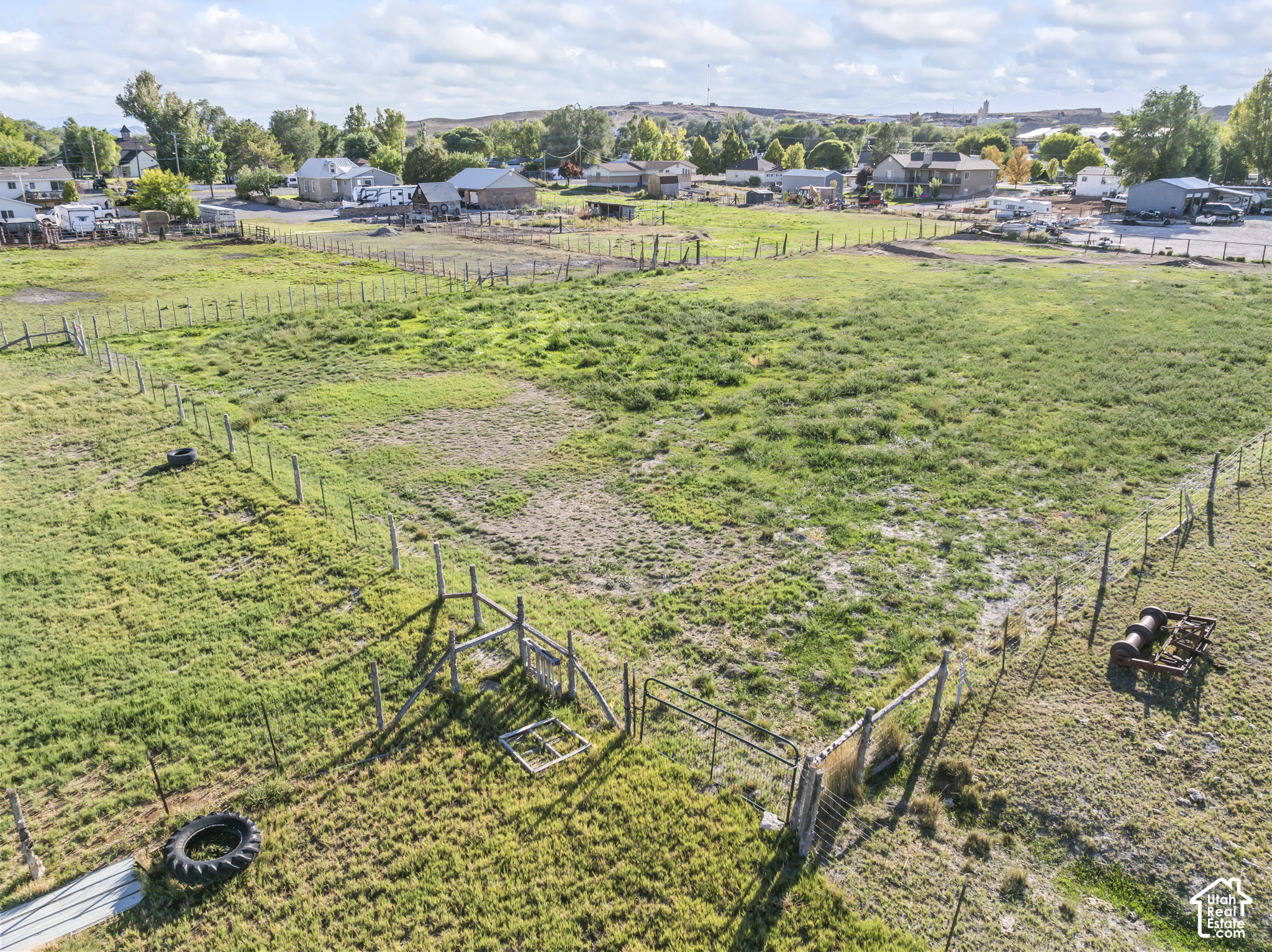 Fenced grassy vacant lot with gates, neighboring homes, and low hills beyond.
