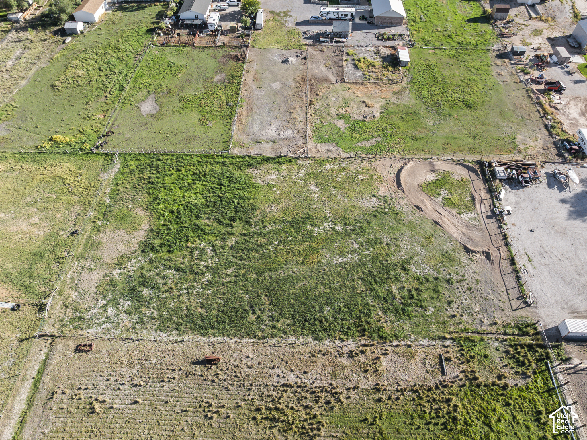 Aerial view of fenced pasture with a curved dirt track and scattered outbuildings.