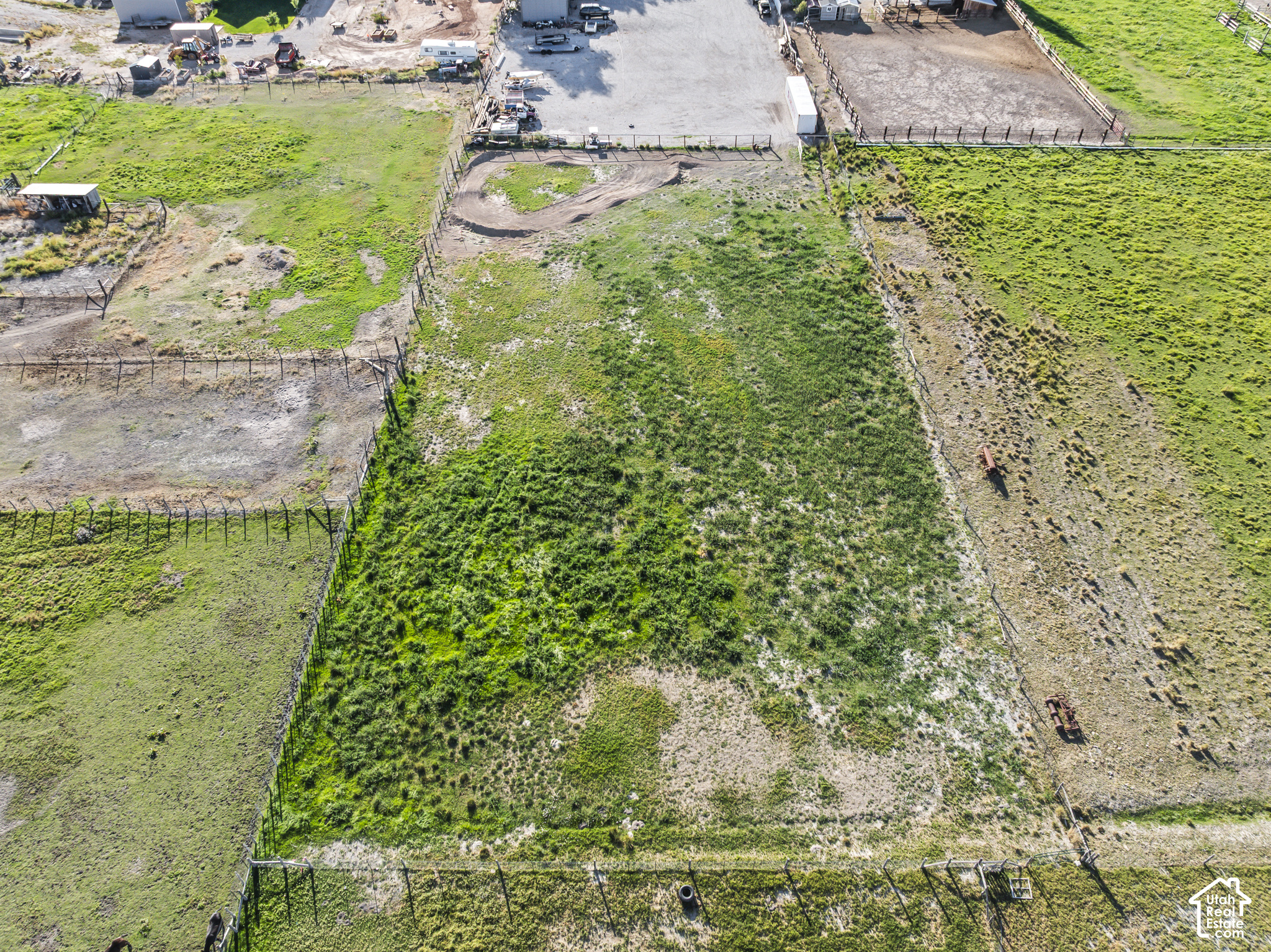 Aerial view of a fenced pasture with patchy green grass and a curved dirt track.
