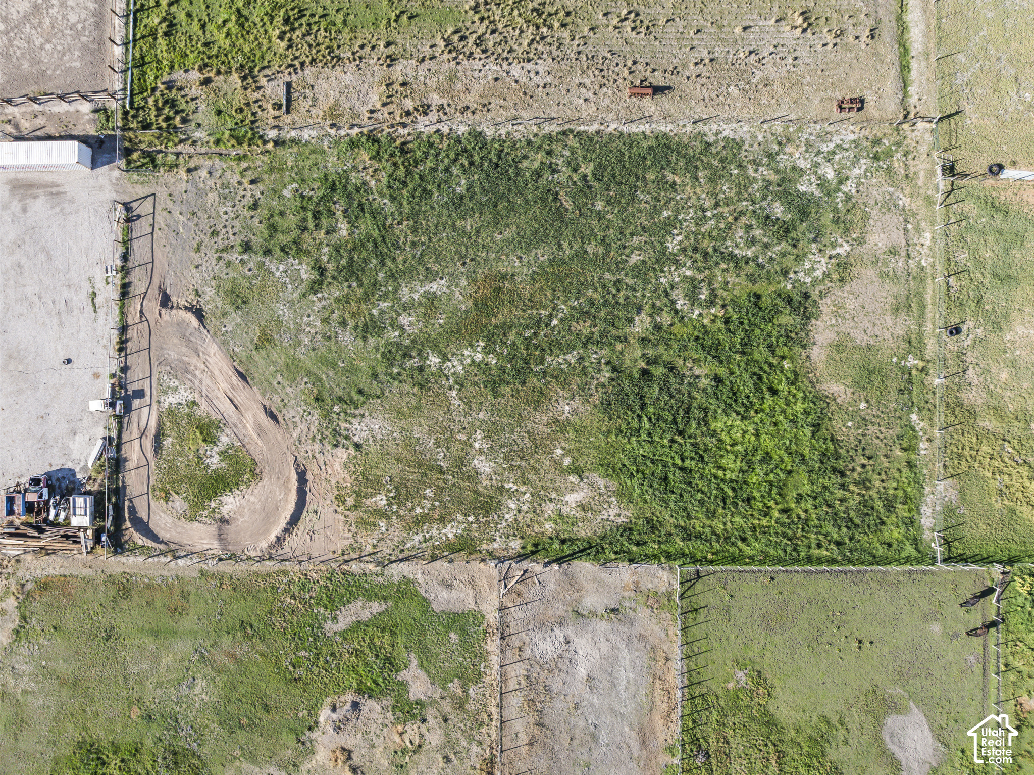 Fenced grassy property with a curved dirt track, viewed from above.