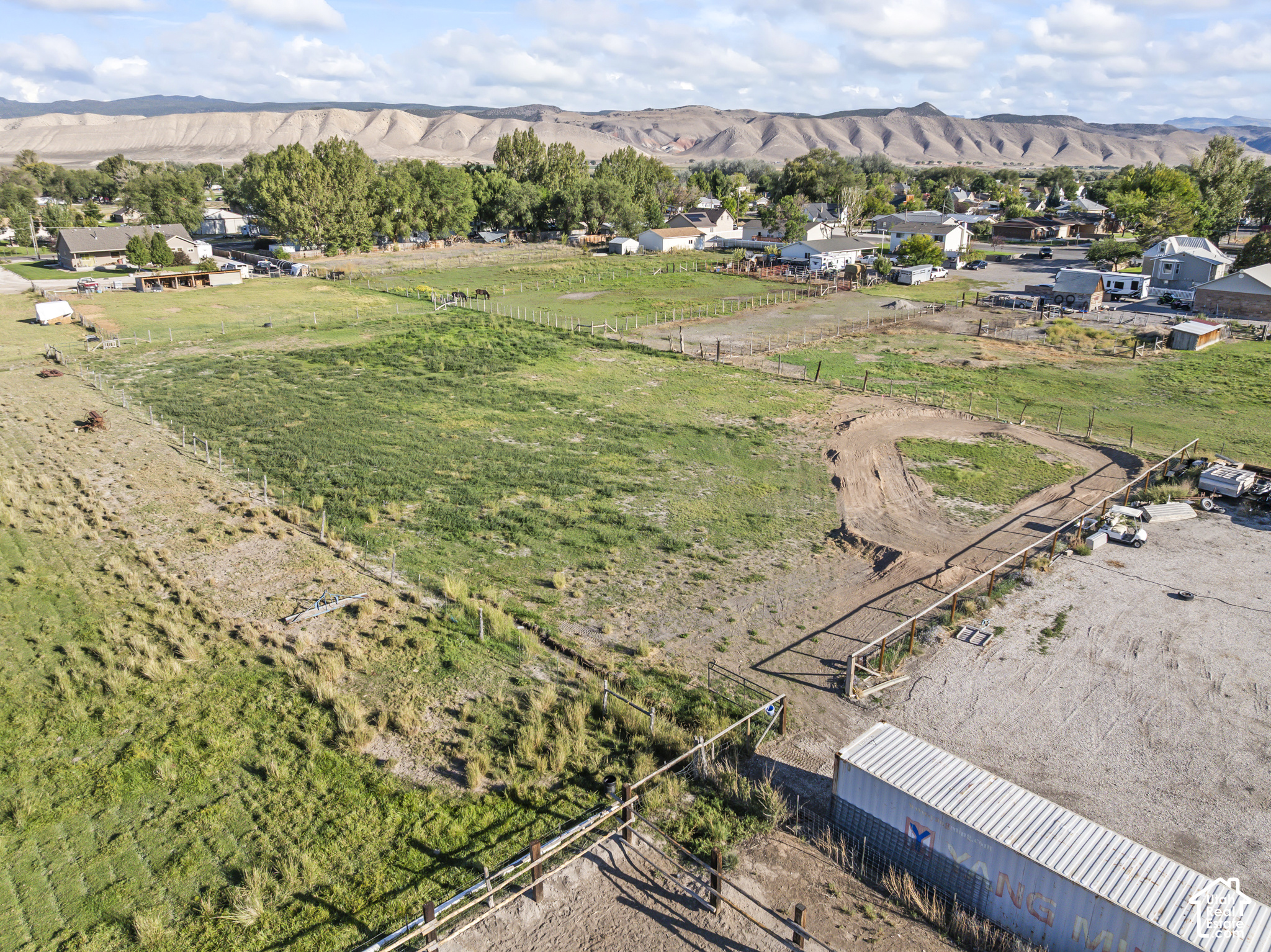 Aerial view of fenced green acreage with nearby homes and pale mountains beyond.