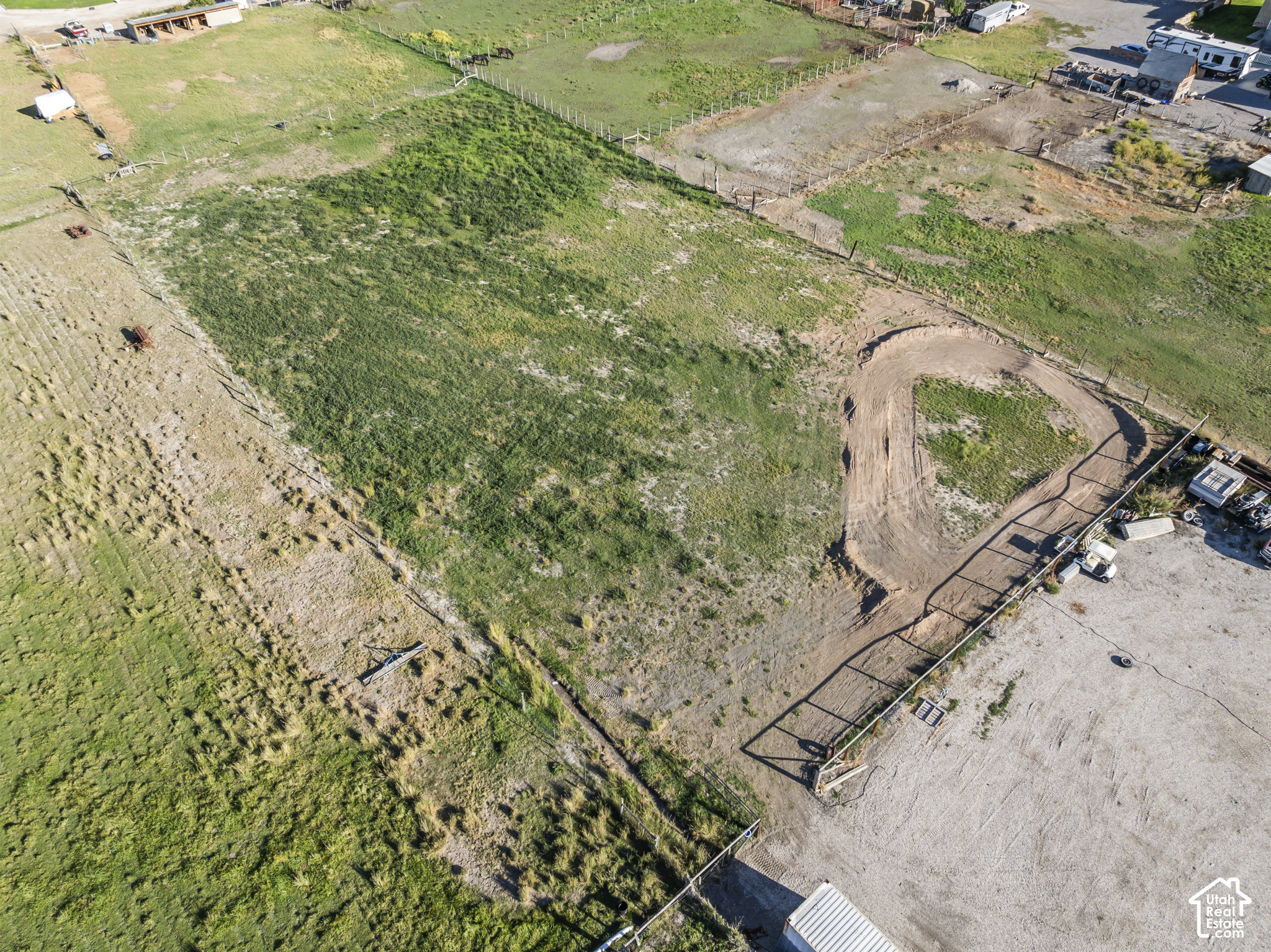 Aerial view of a fenced grassy parcel with a curved dirt track and nearby outbuildings.