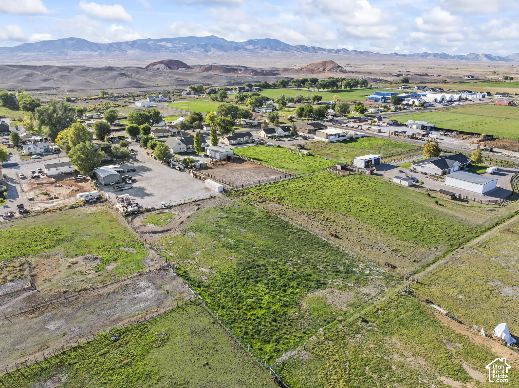 Aerial view of fenced rural pastures and farm buildings, with mountains in the distance.