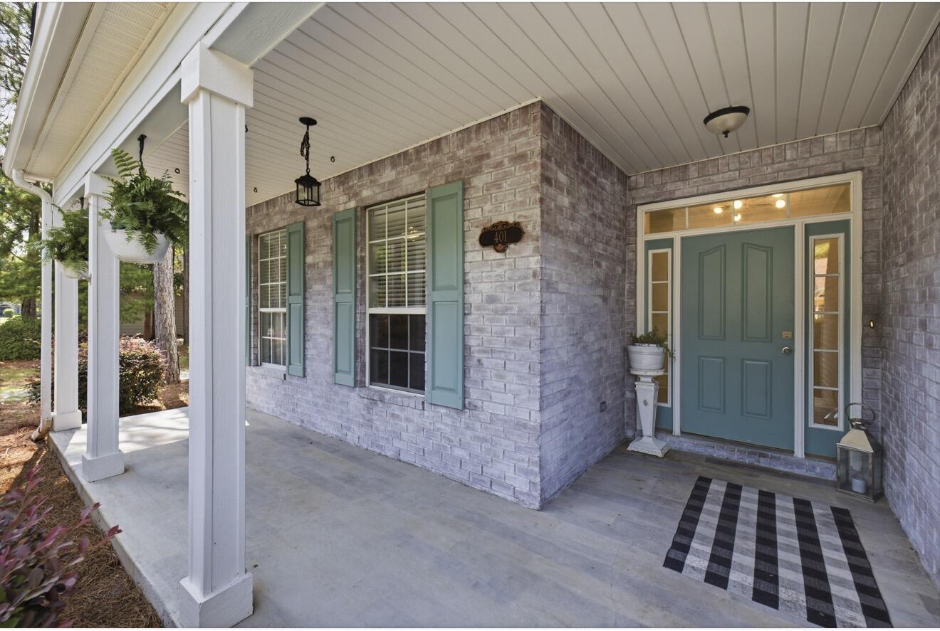 Brick home entrance with a teal double door, matching shutters, white porch columns, and a striped rug.