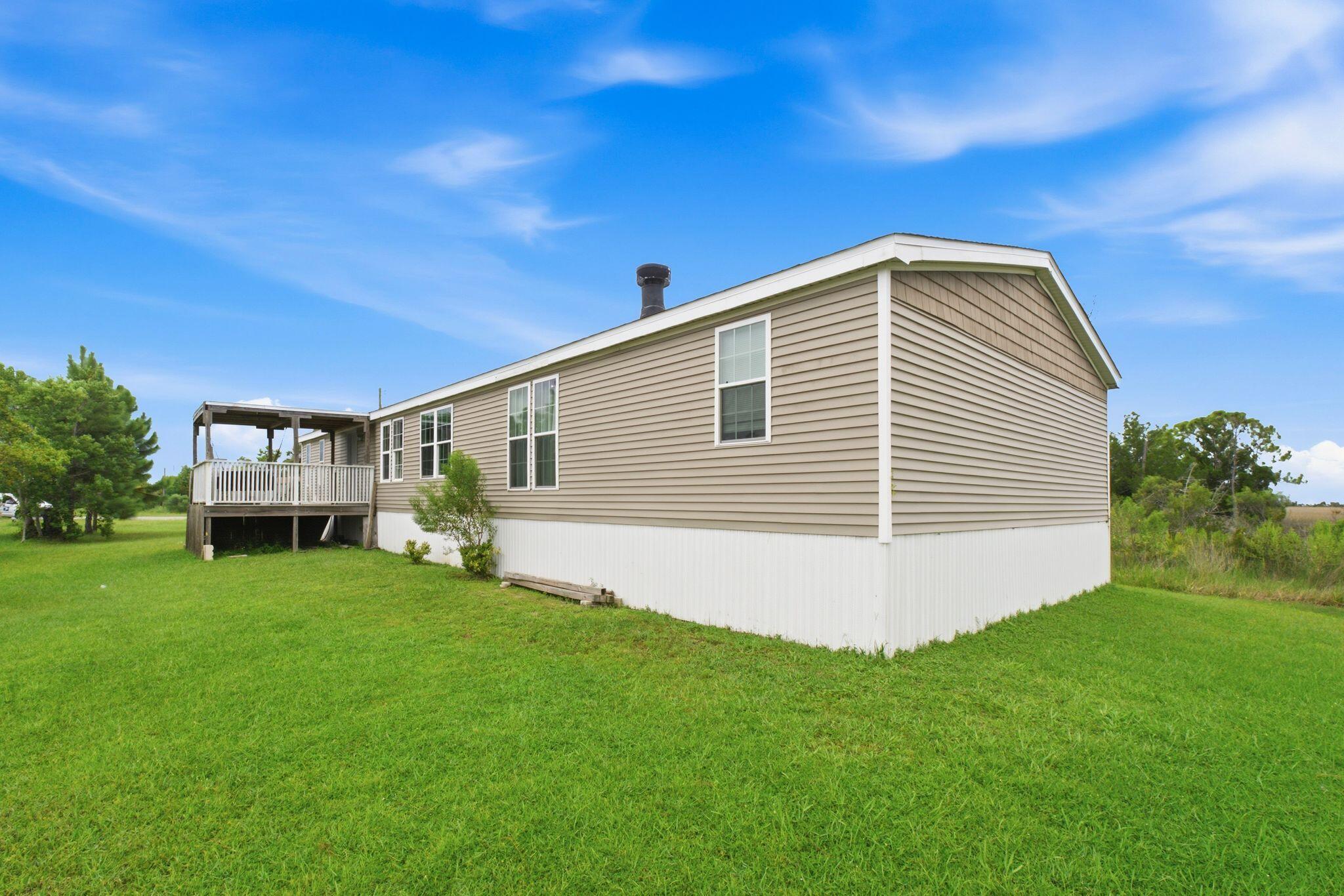 Beige-sided home with a raised deck and white railing beside a broad green lawn.