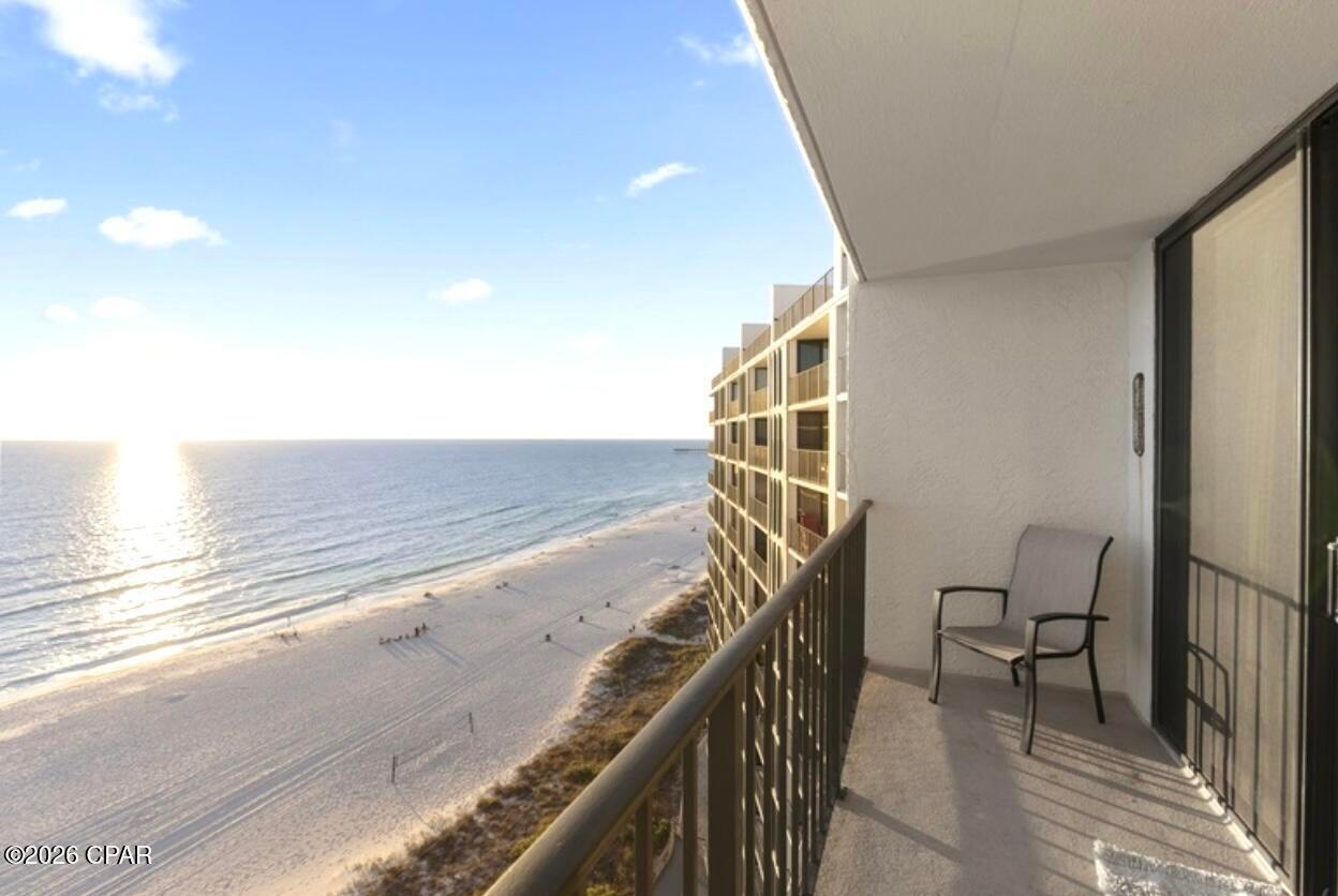Condo balcony with chairs overlooking a sandy beach and sunlit Gulf waters.