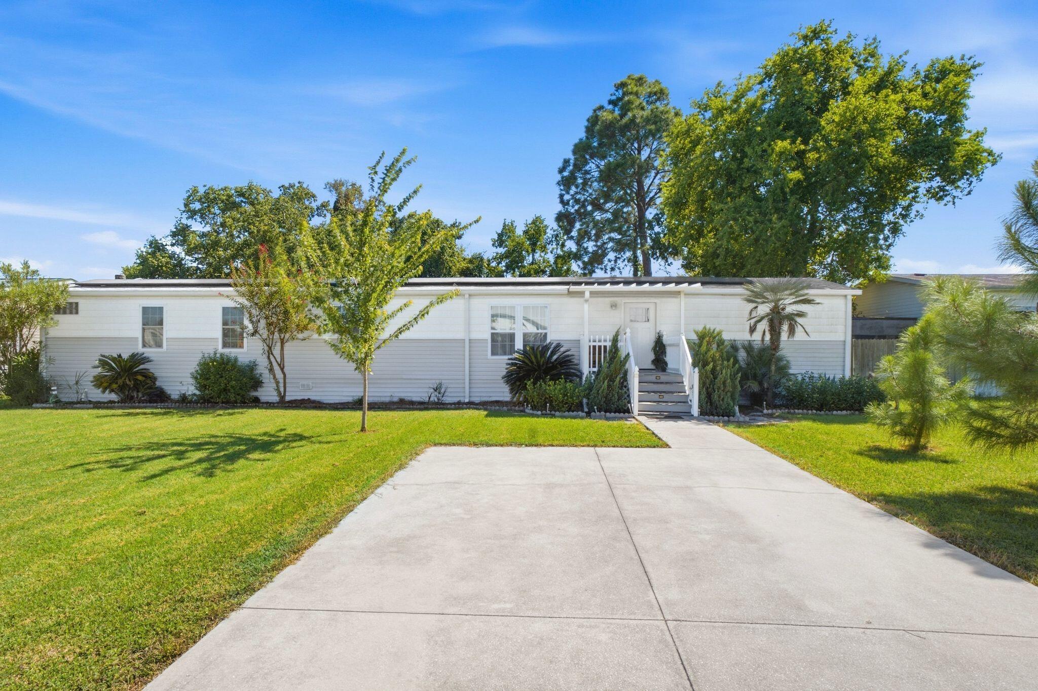 Long white single-story home with a broad driveway, green lawn, and landscaped front entry.
