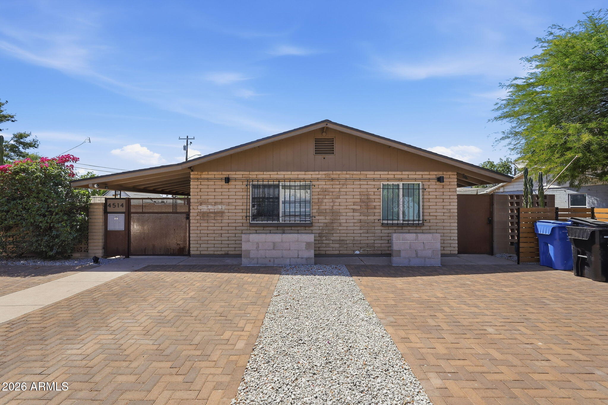Single-story brick house with barred windows, a wide paver driveway, and a gravel path.