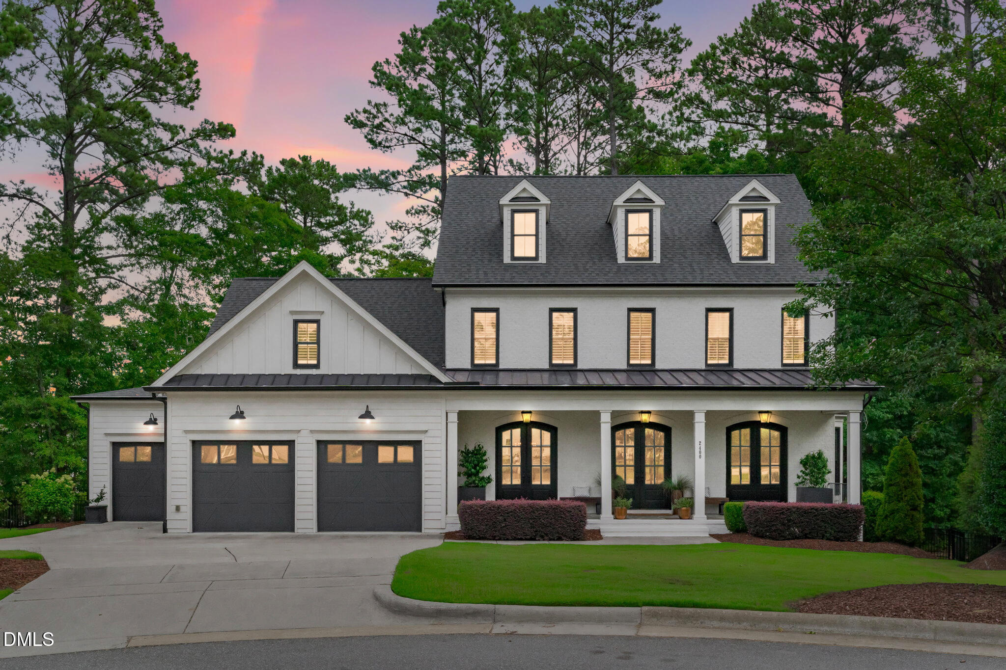 White multi-story house with three garage doors and a covered porch at dusk beneath a pink sky.