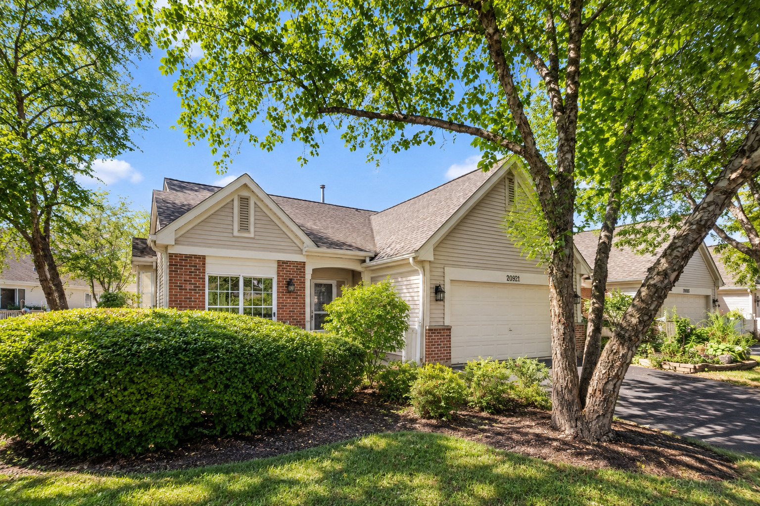 Single-story home with brick accents and an attached garage, framed by mature trees and landscaped shrubs.