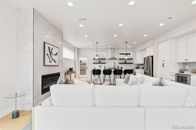 Open-concept living room with a white sectional, marble fireplace, and kitchen island with black stools.