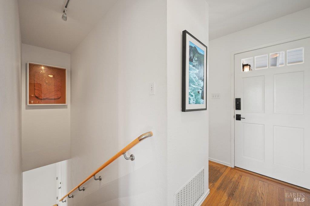 Entry foyer with a white paneled front door, hardwood floors, and a stairway with a wooden handrail.