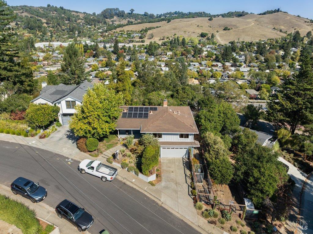 Aerial view of a single-story home with rooftop solar panels amid a hilly neighborhood.