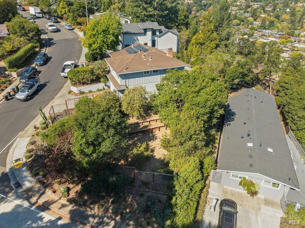 Aerial view of a tree-surrounded home with rooftop solar panels beside a residential street.