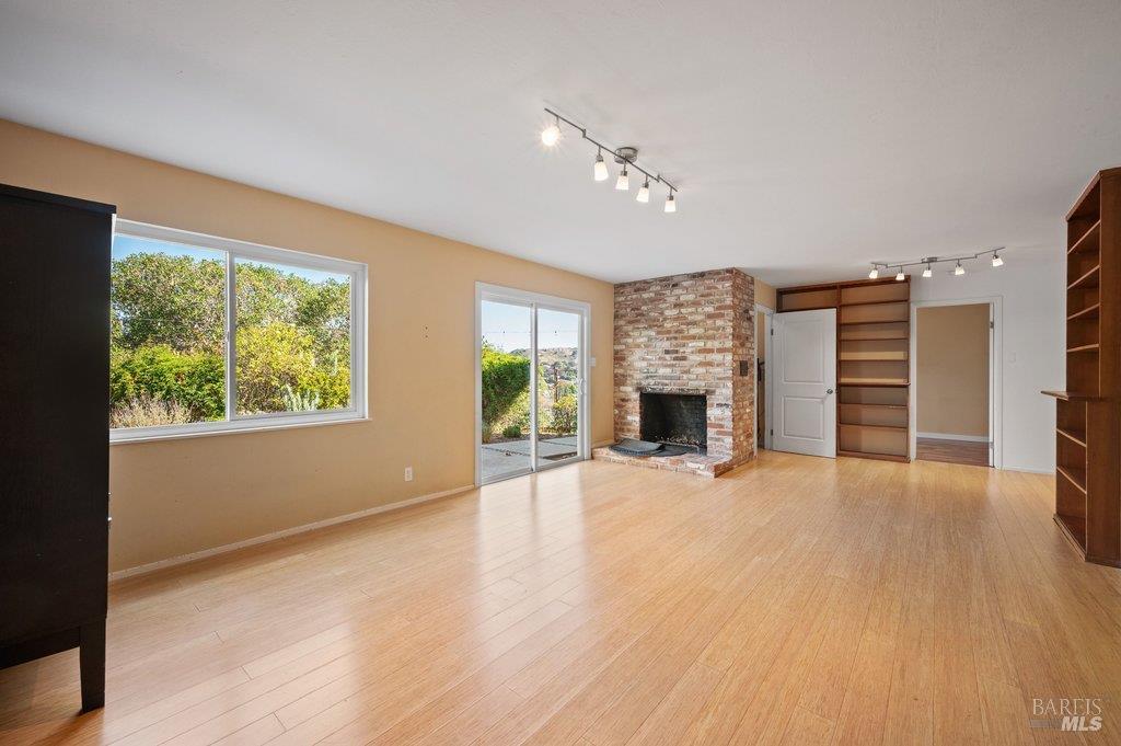 Vacant living room with a brick fireplace, light wood floors, and sliding glass doors to a patio.