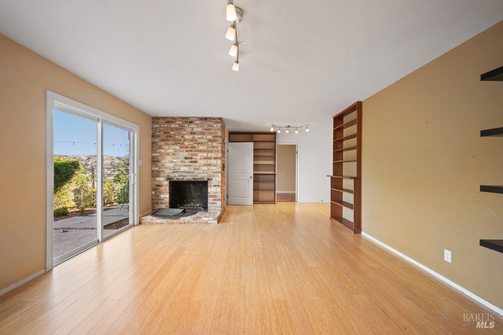 Vacant living room with a brick fireplace, built-in shelves, and sliding glass doors to a patio.