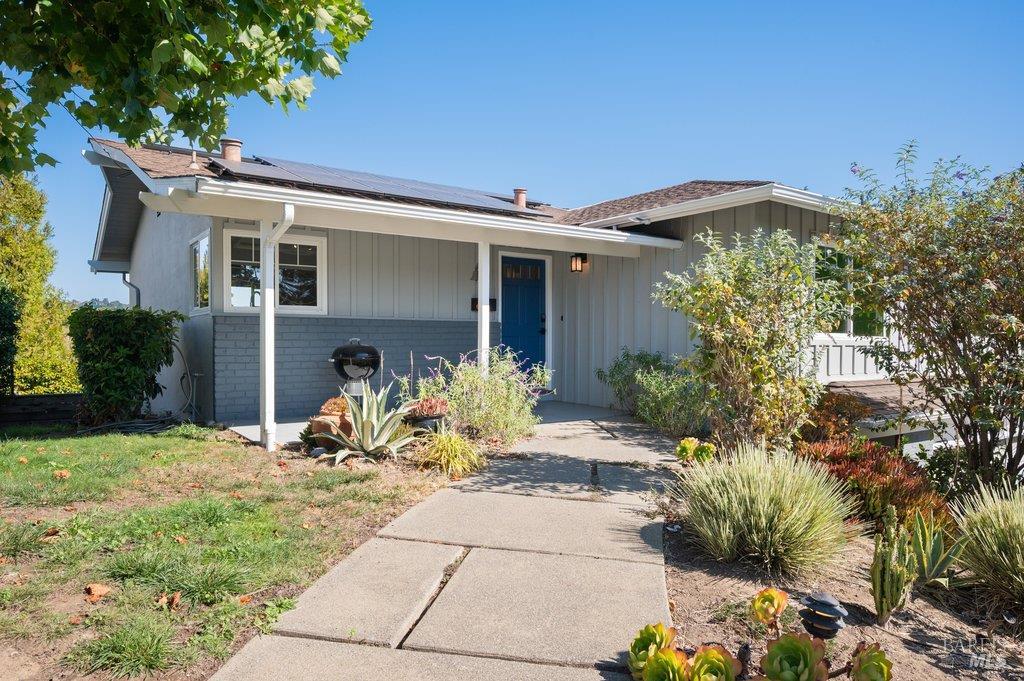 Gray single-story home with solar panels, a blue front door, and a landscaped walkway.