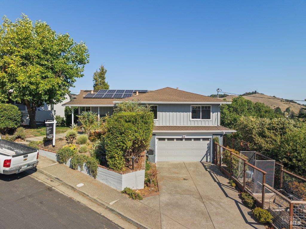 Gray two-story home with rooftop solar panels, a front garden, and a driveway leading to the garage.