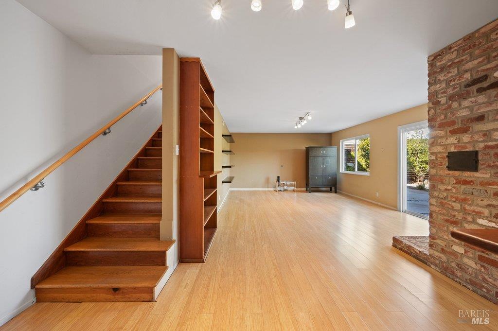 Empty living area with a brick fireplace, built-in shelving, and a wooden staircase.