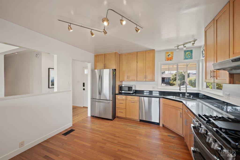 Kitchen with wood cabinetry, black countertops, stainless steel appliances, and hardwood floors.
